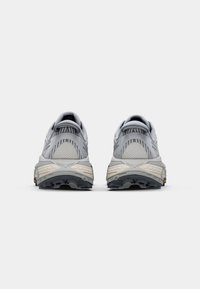 Grau Sport Schuhe mit Mesh- und Netzpaneelen, strukturiertem Fersenbereich und robustem schwarzen Außensohle, die nahe der Ferse einen gelben Akzent aufweist.