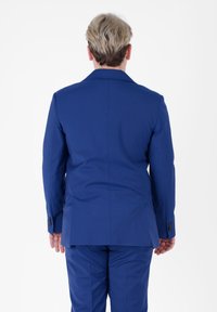 Completo su misura blu con una vestibilità strutturata. La giacca presenta revers affilati e polsini con bottoni, realizzata in un tessuto morbido con una leggera lucentezza.