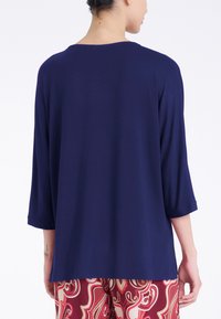 Top blu navy a maniche tre quarti con vestibilità rilassata e scollo rotondo, realizzato in un tessuto leggero e morbido; senza motivi o accessori visibili.