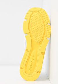 Semelle de sneaker blanche avec un fond en caoutchouc jaune texturé comportant des motifs triangulaires et le mot "ABZORB" en relief. Bords et design lisses.