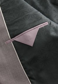 Gepatchter Stoff mit einem geometrischen Muster in Dunkelgrün, ausgestattet mit einem strukturierten grauen Abschnitt und einer lila dreieckigen Tasche. Mit einem hellen Rand versehen.