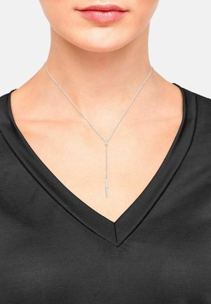 Collana con pendente d'argento e catena sottile, caratterizzata da un design a goccia elegante e allungato. Indossata sopra un top nero a V.