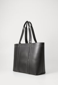 Svart läder tote-väska med två tjocka handtag, med kontrasterande vit sömnad och präglad "HUGO"-logotyp på sidopanelerna.