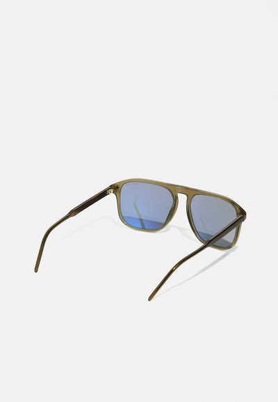 Saulesbrilles ar kvadrātu formu, olīvu zaļas plastmasas rāmi un zilo gradienta lēcu. Plānas, tumšas metāla kājas, elegants dizains, atstarojot virsma.