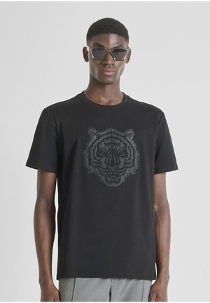 Camiseta de algodón negra con un gráfico tridimensional de la cabeza de un tigre en gris oscuro en el frente. Mangas cortas y cuello redondo.