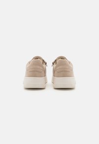 Adidași bej din suede cu o suprafață texturată și tălpi din cauciuc alb, având un spate neted și fermoare laterale pentru acces ușor.