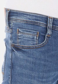 Jeans de mezclilla azul con un diseño clásico, que cuentan con costuras naranjas, un bolsillo trasero y una etiqueta de cuero en la cintura.