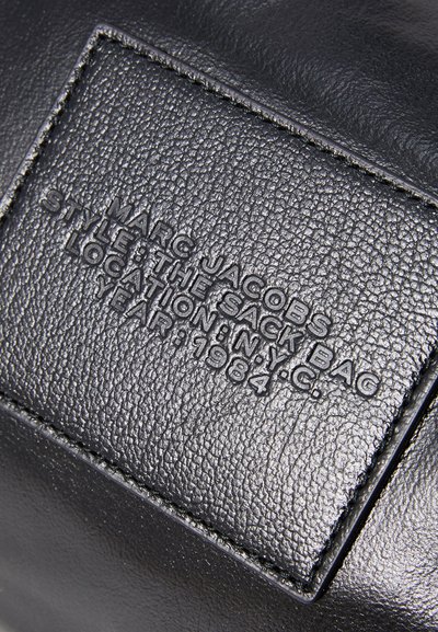 Musta tekstuuriga nahktasku, millel on reljeefne silt, kus on kirjas "MARC JACOBS", "STIIL: THE SACK BAG" ja "AASTA: 1984."