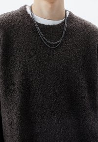 Felpa in pile grigio scuro con superficie testurizzata, dotata di scollatura rotonda e abbinata a una collana d'argento a strati.