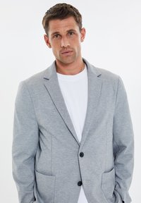 Szary żakiet wykonany z teksturowanej tkaniny, z klapami, dwiema przednimi kieszeniami i zapięciem na pojedynczy guzik na białym t-shircie.