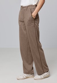 Pantalons marron texturés avec deux poches avant, une fermeture à un bouton et une coupe droite. Associés à des baskets blanches.