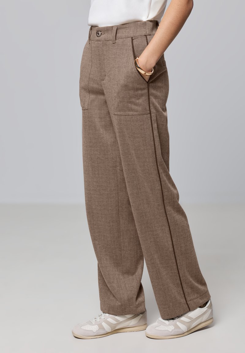 Pantalons marron texturés avec deux poches avant, une fermeture à un bouton et une coupe droite. Associés à des baskets blanches.