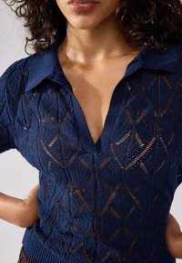 Pullover in maglia navy con scollo a V e colletto, caratterizzato da una tessitura a rete aperta con motivo a rombi. Tessuto testurizzato con dettaglio a costine sull'orlo.