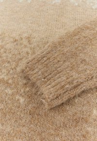 Maglione lavorato a maglia in un morbido filato marrone chiaro. Presenta un motivo testurizzato e polsini a costine. Il tessuto appare sfocato e trasmette una sensazione di calore e comodità.