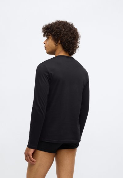 Camisa preta de manga longa feita de tecido suave, com decote redondo e mangas ajustadas, vista por trás. Design simples e sem costuras.