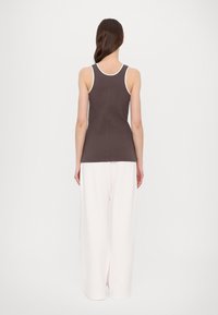 Braunes geripptes Tanktop mit weißem Saum, kombiniert mit lockeren weißen Hosen, die ein einfaches Design und eine glatte Textur zeigen.