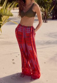 Haut de bikini tricoté vert associé à un pantalon large rouge à motifs vifs, orné de tourbillon, de motifs floraux et d'une ceinture rayée.