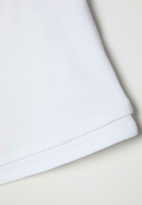 Tissu en coton blanc plié avec des coutures doubles visibles le long des bords sur un fond clair.