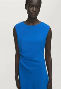 Vestido sin mangas azul con escote redondo, tela drapeada y textura suave, que presenta una silueta ajustada y un sutil detallado en los laterales.