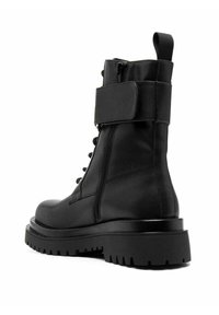 Bota de combate negra con un upper sintético texturizado, diseño de cordones en la parte frontal, cremallera lateral y una suela gruesa y robusta con un dibujo pronunciado.