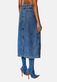Denim midi-rok met een rechte snit, rafelige zoom en een split aan de achterkant. Draagt blauwe kniehoge laarzen en puntige hakken met een metallic accent.