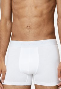 Boxers en coton blanc avec une taille élastique douce arborant une marque discrète. Texture lisse et design ajusté, mettant l'accent sur le confort.
