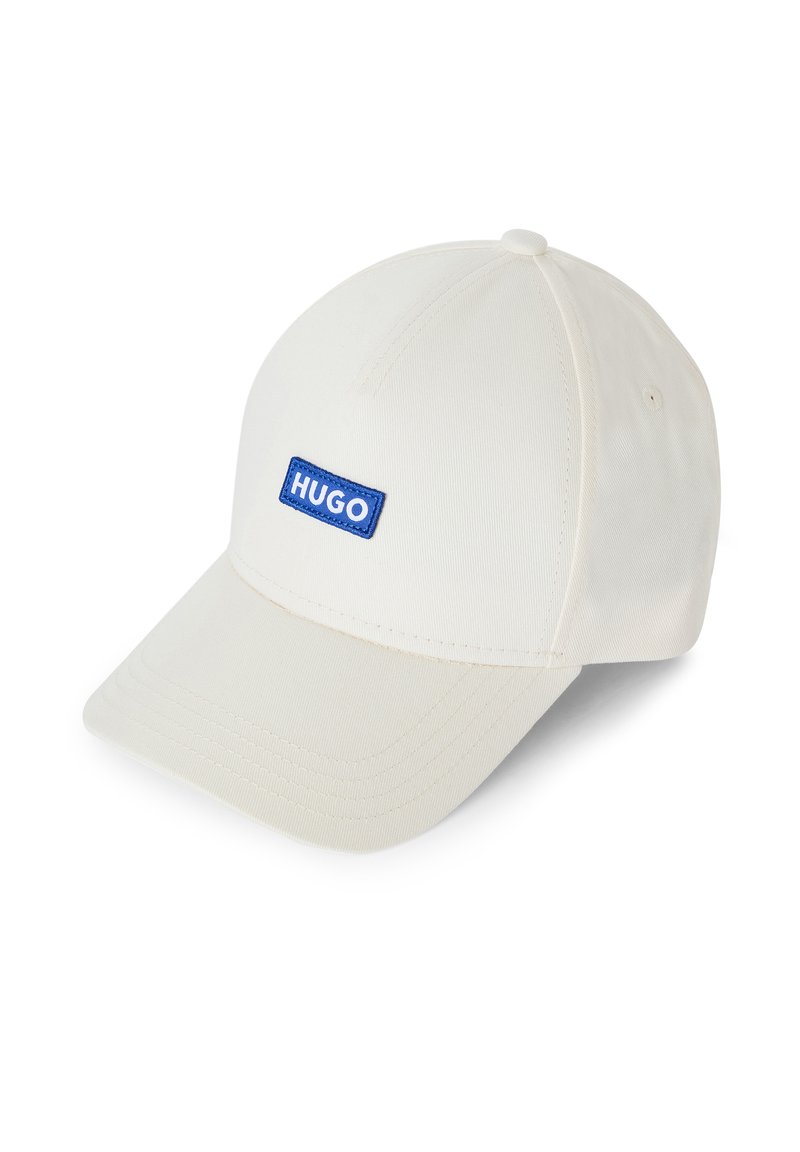Witte baseballcap van katoen, voorzien van een blauwe rechthoekige patch met het woord "HUGO." De gebogen rand en de gestikte details zijn zichtbaar.