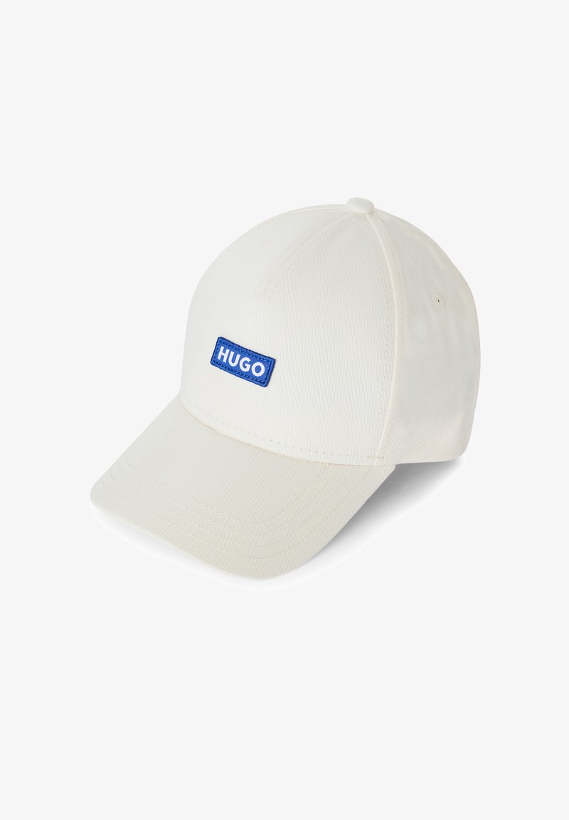 Cappello da baseball bianco in cotone, con una toppa rettangolare blu recante la scritta "HUGO". La visiera curva e i dettagli cuciti sono ben visibili.