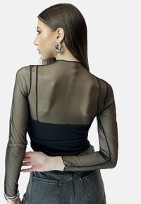 Schwarzes Mesh-Oberteil mit langen Ärmeln, transparentem Rücken und Ärmeln; figurbetontes Design, strukturierter Stoff und dezente Nähte. Akzente in Grautönen.