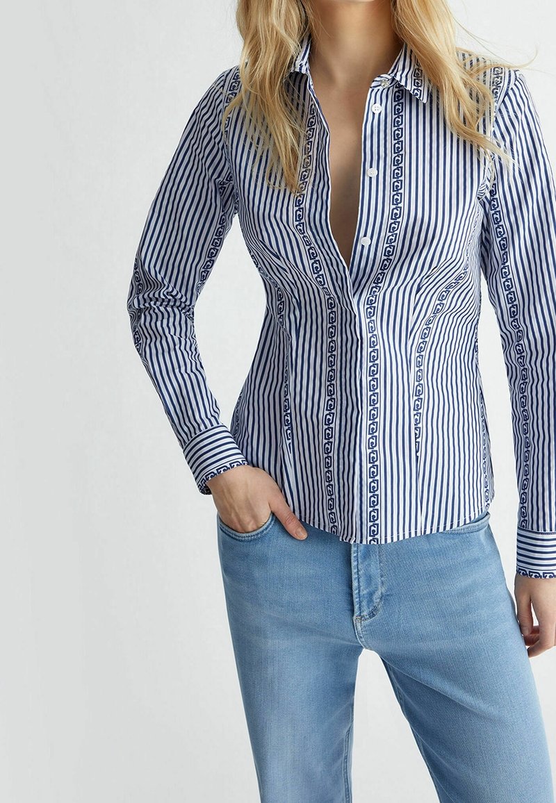 Randig skjorta i blått och vitt, med ett mönstrat knäppband och manschetter, långärmad och figursydd. Bärs med blå jeans.