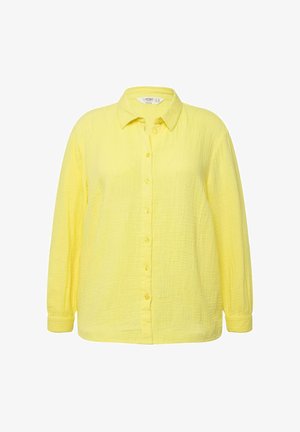 Gul skjorte med knaplukning lavet af tekstureret stof, med krave og lange ærmer med knappede manchetter. Jævnt placerede knapper ned ad fronten.