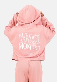 Hoodie corto rosa con una grande grafica testuale bianca sulla schiena. Tessuto morbido, maniche lunghe e un cappuccio ampio.