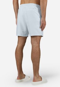 Lyseblå badeshorts med elastisk midjebånd, baklomme og jevn tekstur, kombinert med hvite sandaler.