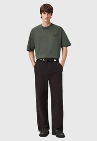 Vihreä oliivi puuvillapaita leveällä istuvuudella ja lyhyillä hihoilla, yhdistetty mustiin suoriin housuihin ja tummiin kenkiin. Mukana hopeaketjukaulaketju.