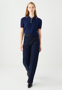 Polo a righe blu navy con dettagli in bianco e rosso, abbinato a pantaloni in denim scuro a vita alta con tasche frontali e taglio dritto.