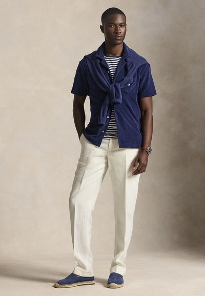 Ναυτικό μπλε φανελένιο πουκάμισο με ριγέ μπλούζα από μέσα, ανοιχτόχρωμο παντελόνι από λινό και μπλε εσπαντρίγιες με πλεκτές λεπτομέρειες.