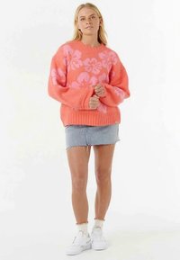 Knitted sweater in bright coral with pink floral pattern, relaxed fit, ribbed hem, worn with a denim mini skirt and white sneakers.