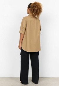 Light brown collared shirt with rolled sleeves, paired with loose-fitting black cargo pants featuring side pockets and a relaxed silhouette.