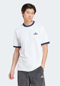Fehér pamut póló sötétkék bordás nyakkal és ujjakon. A mellkasán kis sötétkék Adidas logó található. Laza fazon.