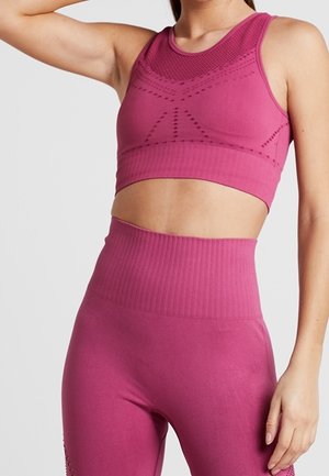 Kvinde iført matchende lyserød sømløs sports-bh og høj-taljede leggings med tekstureret mønster, poserer med den ene arm hævet.