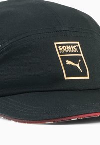 Sort kasket med en flad skygge, der har et guld "SONIC THE HEDGEHOG" logo og Puma logo. Indersiden viser et mønstret rødt stof.
