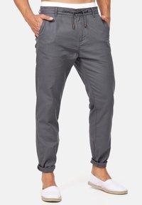 Pantaloni in misto cotone grigi con vita elasticizzata e coulisse, due tasche laterali e orli arrotolati, abbinati a scarpe bianche slip-on.