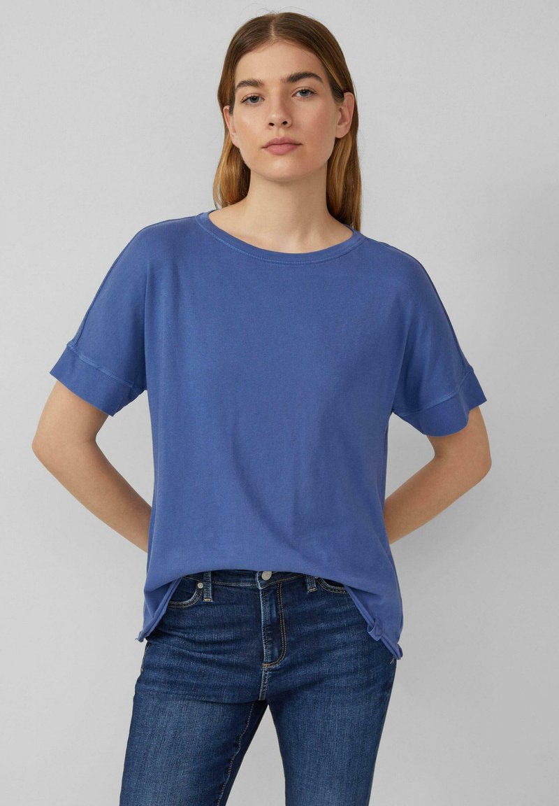 Blauw T-shirt met korte mouwen en een ronde hals, relaxte pasvorm en opgerolde mouwen. Zachte stof met een gladde textuur. Gecombineerd met donkere jeans.