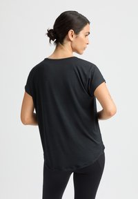 Top nero a maniche corte con vestibilità rilassata, scollo rotondo e orlo curvo. Realizzato in tessuto morbido, presenta una texture liscia e una leggera lucentezza.