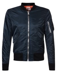 Veste bomber bleu marine en tissu brillant, avec une fermeture éclair à l'avant, des poches latérales et un ourlet et des poignets côtelés. Poche à zip notoire sur le bras.