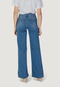 Jeans de cintura alta y pernera ancha en denim azul medio con una textura suave, que cuentan con bolsillos traseros y una cintura con cinturón.