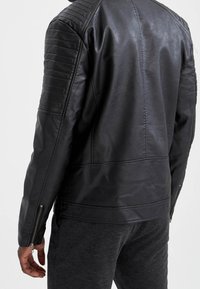 Blouson en cuir noir à finition texturée, avec des accents matelassés aux épaules et des poignets zippés, conçu pour une coupe ajustée.