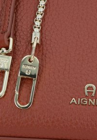 Bolso de mano rojo de cuero texturizado con una correa de cadena plateada y detalles en hardware dorado, incluyendo un logo y un cierre.