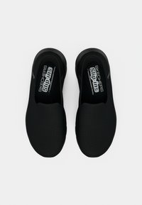 Μαύρα slip-on παπούτσια με αναπνεύσιμο πλέγμα στο επάνω μέρος και μαλακή, επενδυμένη σόλα. Φέρουν το λογότυπο Skechers στην εσωτερική σόλα και στην πλευρά. Λείο υφή.