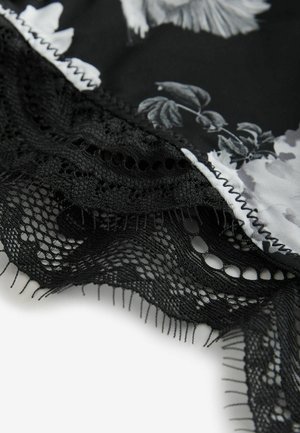 Black fabric with floral print and scalloped, intricate black lace trim with fine fringe edges on a light background.